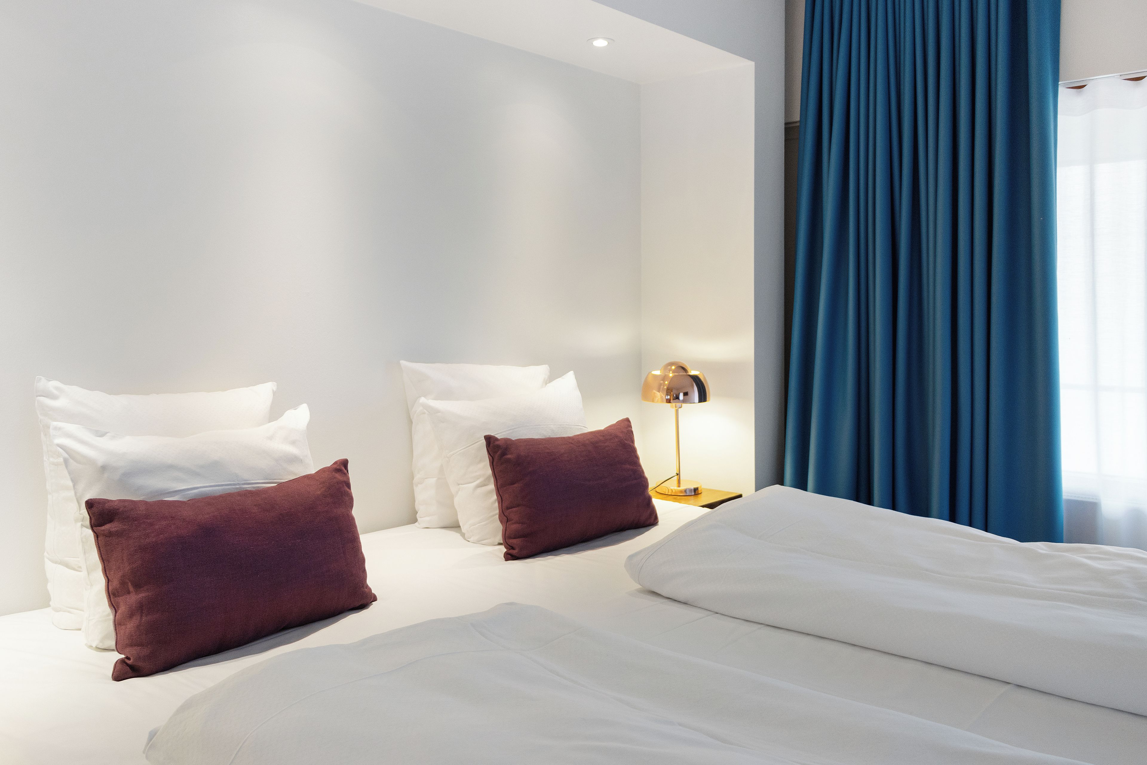 Una habitación de hotel con una cama, almohadas, una mesita de noche y una lámpara.