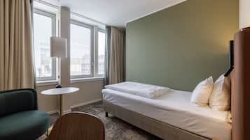 Una habitación de hotel con una cama, una silla, una mesita y una lámpara.