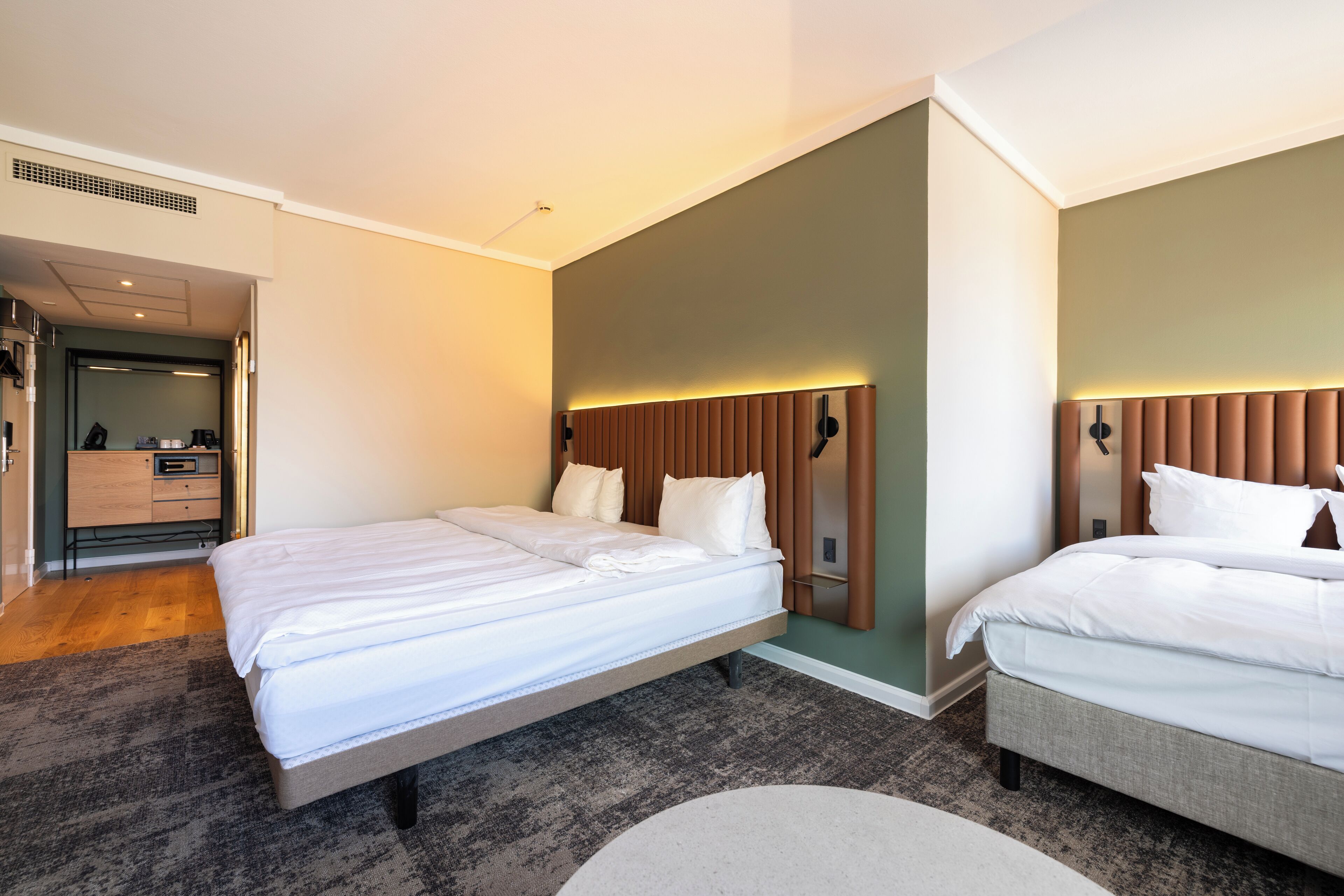A hotel room with two beds, a wooden headboard, and a small desk with a chair.