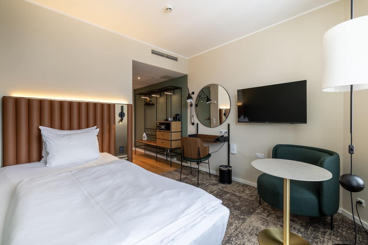 A hotel room with a large bed, a desk with a chair, a television, and a small table.