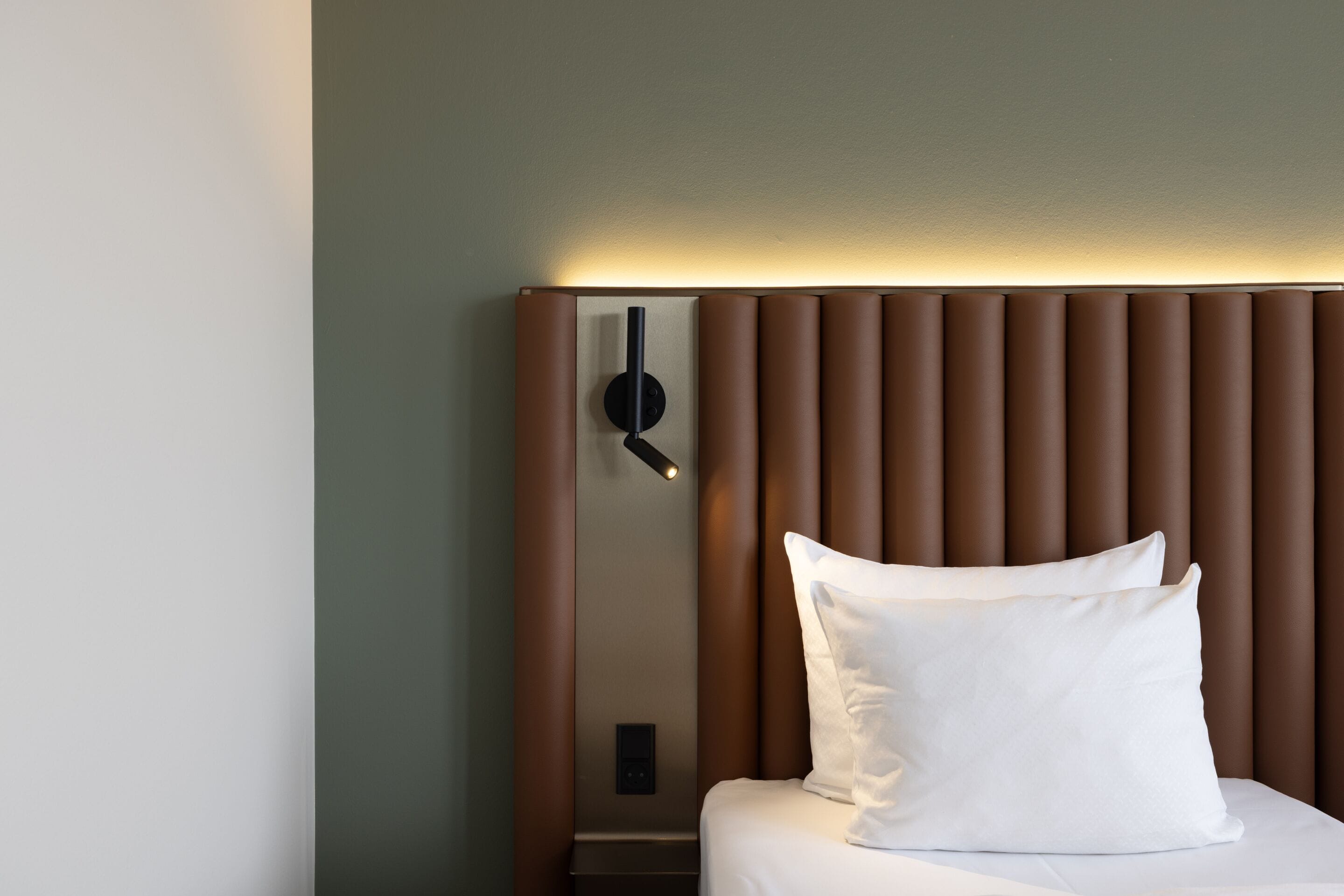A modern hotel room with a bed, a wall-mounted clock, and a bedside table.