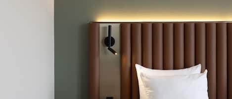 A modern hotel room with a bed, a wall-mounted clock, and a bedside table.