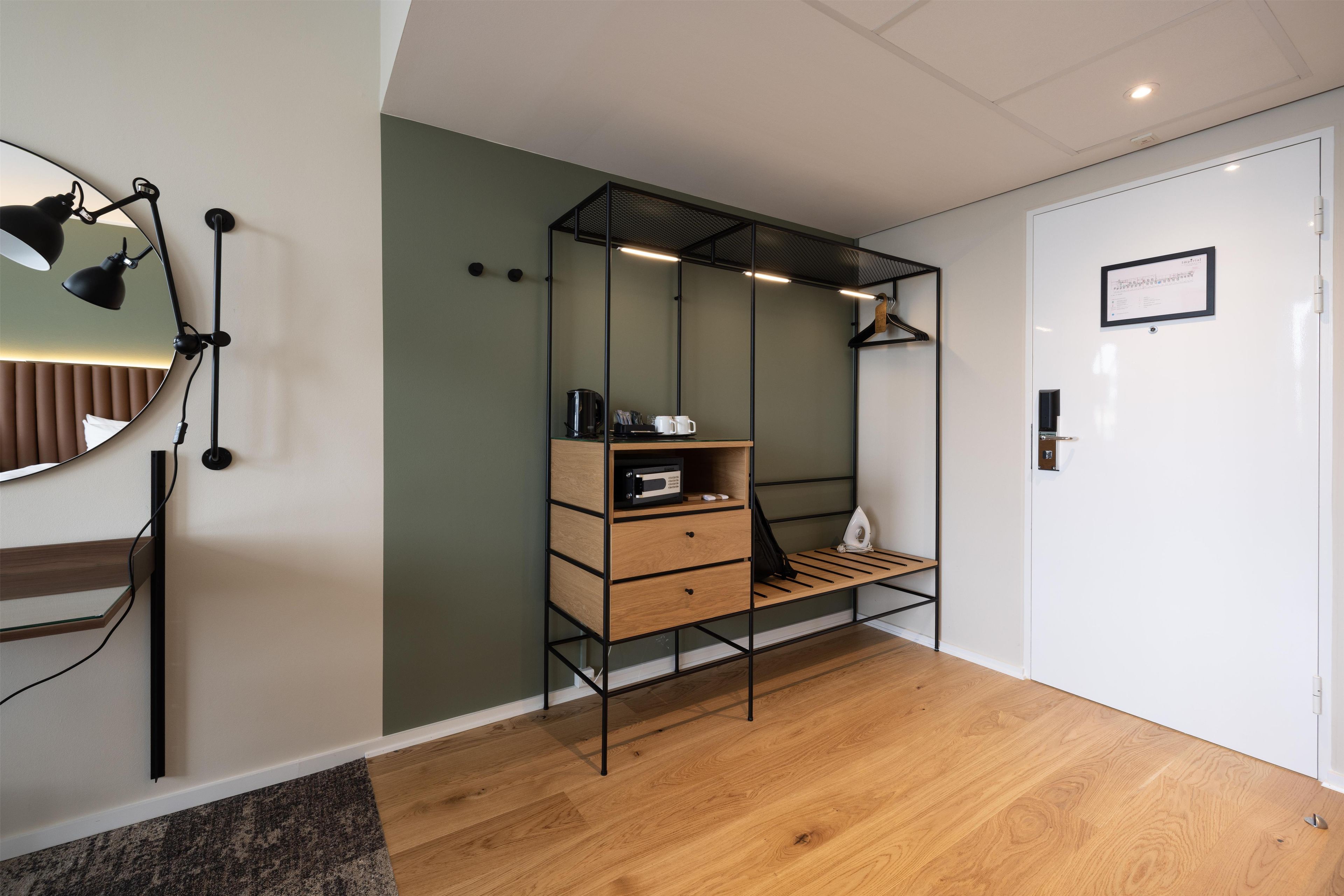 Une chambre moderne avec un plancher en bois, un bureau avec une chaise, un luminaire suspendu et une porte ornée d’un certificat encadré.