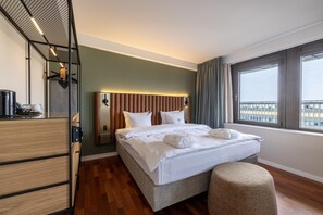 Una habitación de hotel con cama, mesita de noche, ventana con cortinas y vistas a la ciudad.