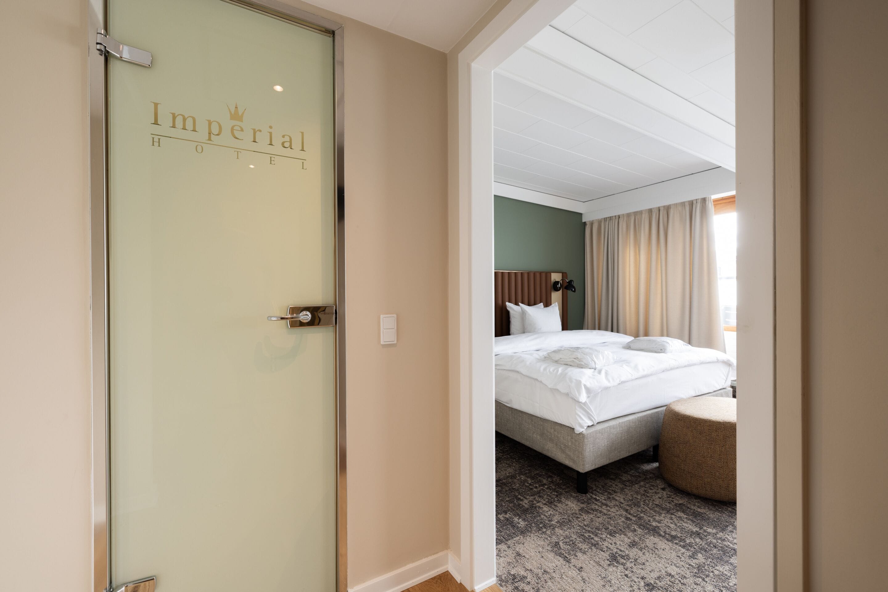 Una camera d'albergo con un letto, un comodino e una porta vetrata con il nome dell'hotel.