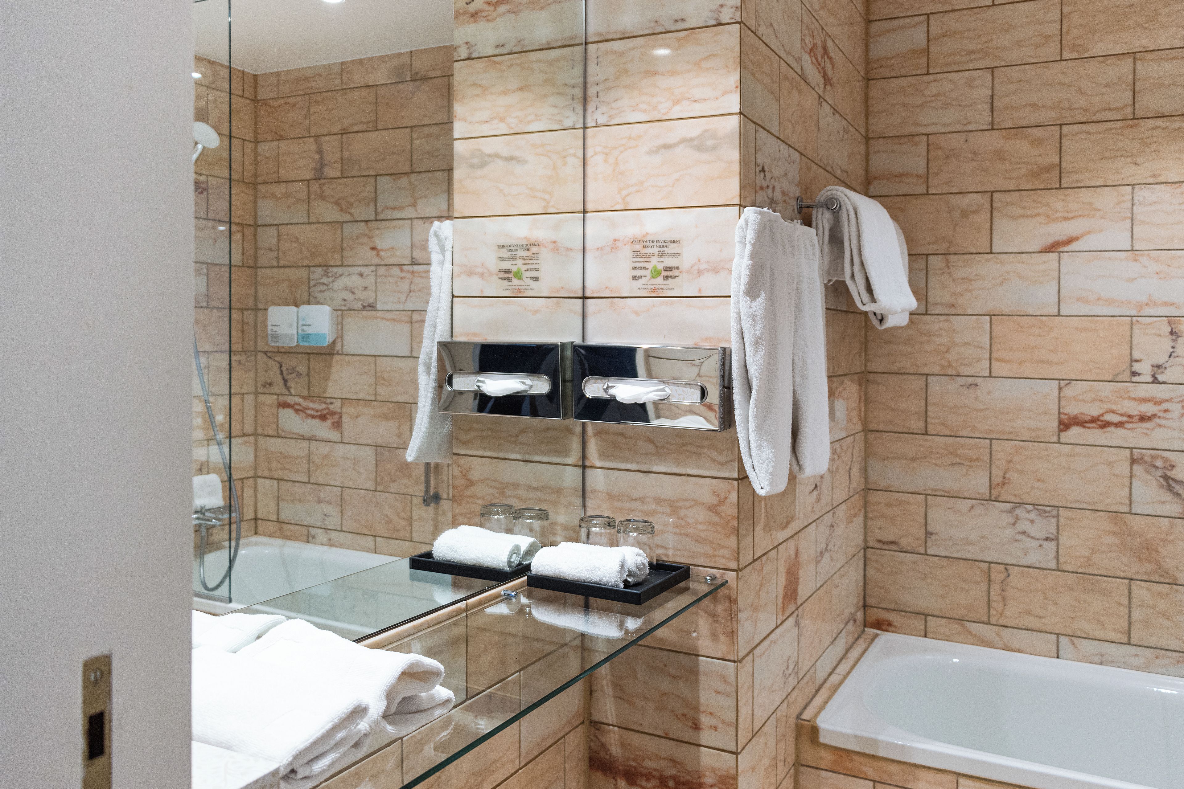 A modern bathroom with a glass-enclosed shower, a glass-topped vanity, and a white bathtub.