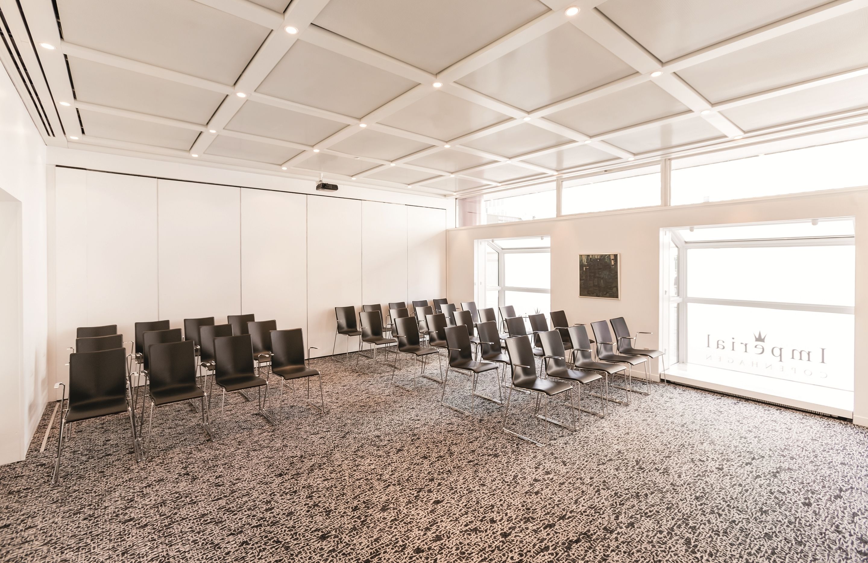 A conference room with a patterned carpet, white ceiling, and a large window with the text "Impressivity".