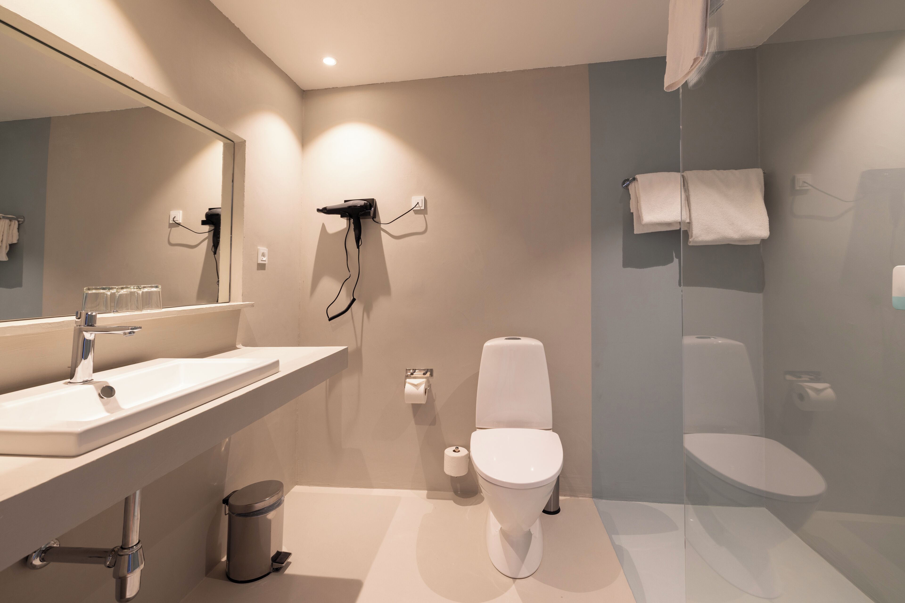 Ein modernes Badezimmer mit großem Spiegel, Waschbecken, Toilette und Duschbereich.