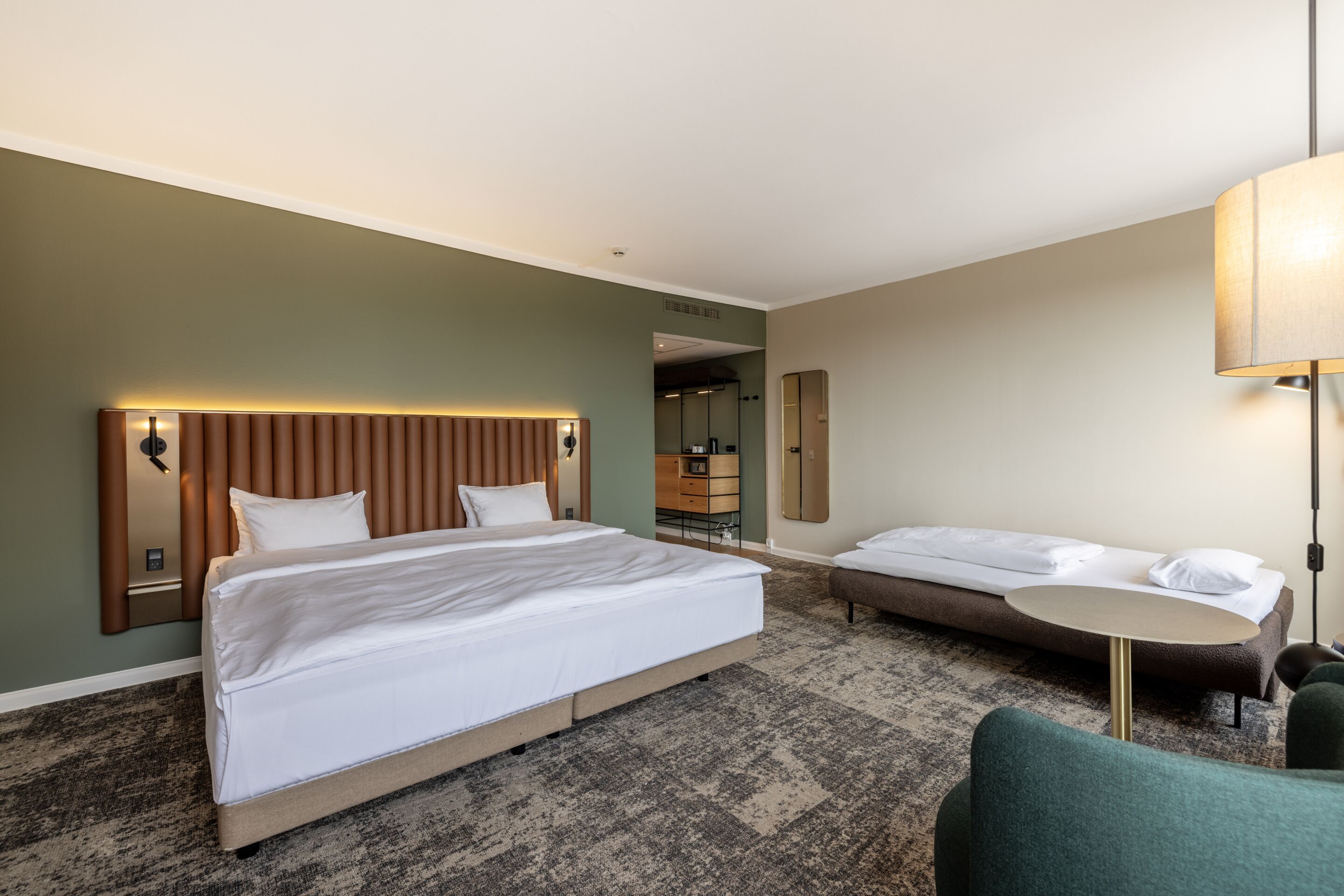 Een hotelkamer met een groot bed, een kleiner bed, een bureau en een stoel.
