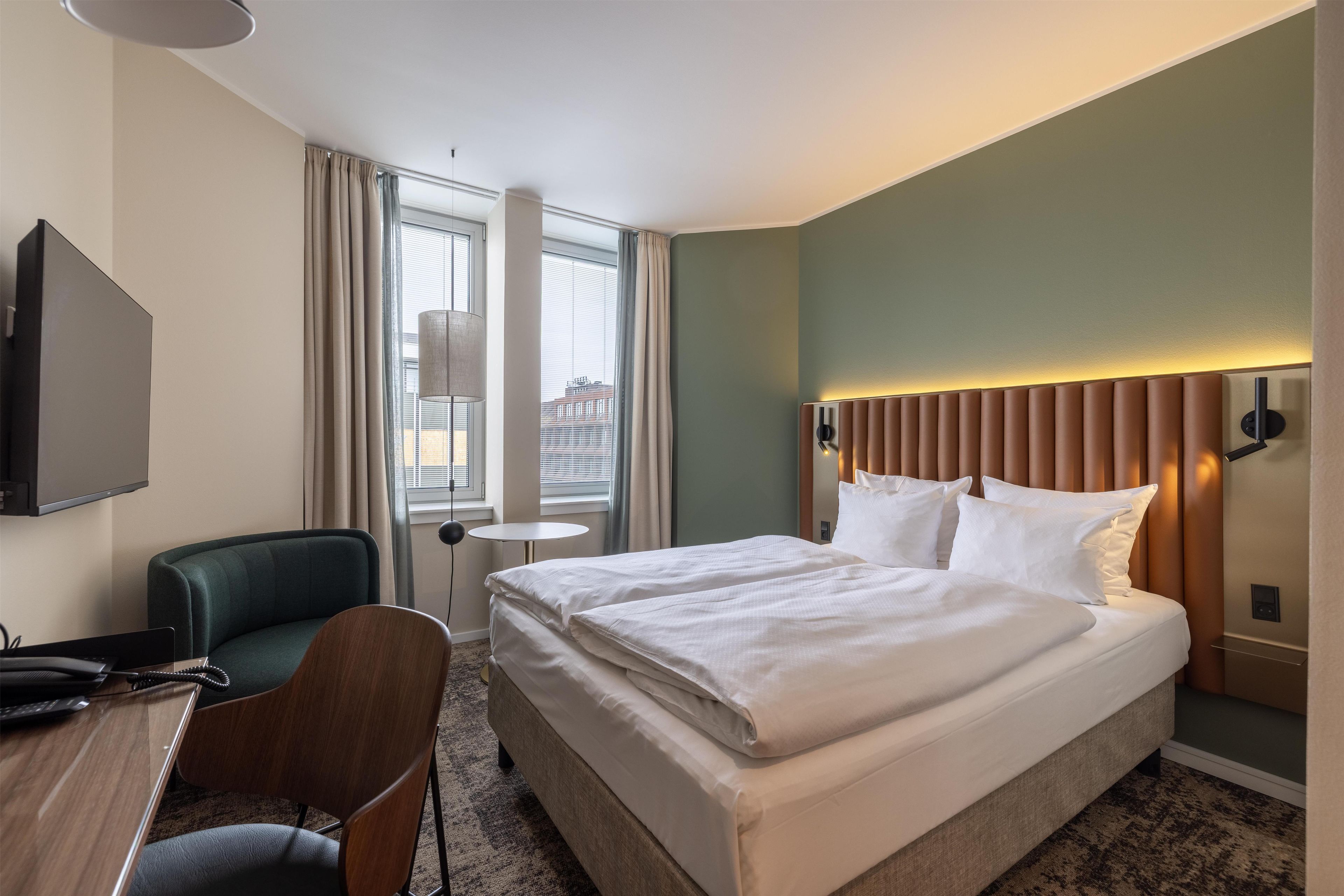Een hotelkamer met een bed, een bureau, een stoel, een televisie en een raam met gordijnen.