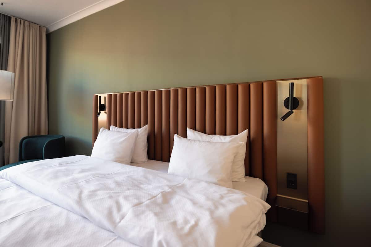 A hotel room with a large bed, a headboard with vertical slats, and a bedside table with a lamp.