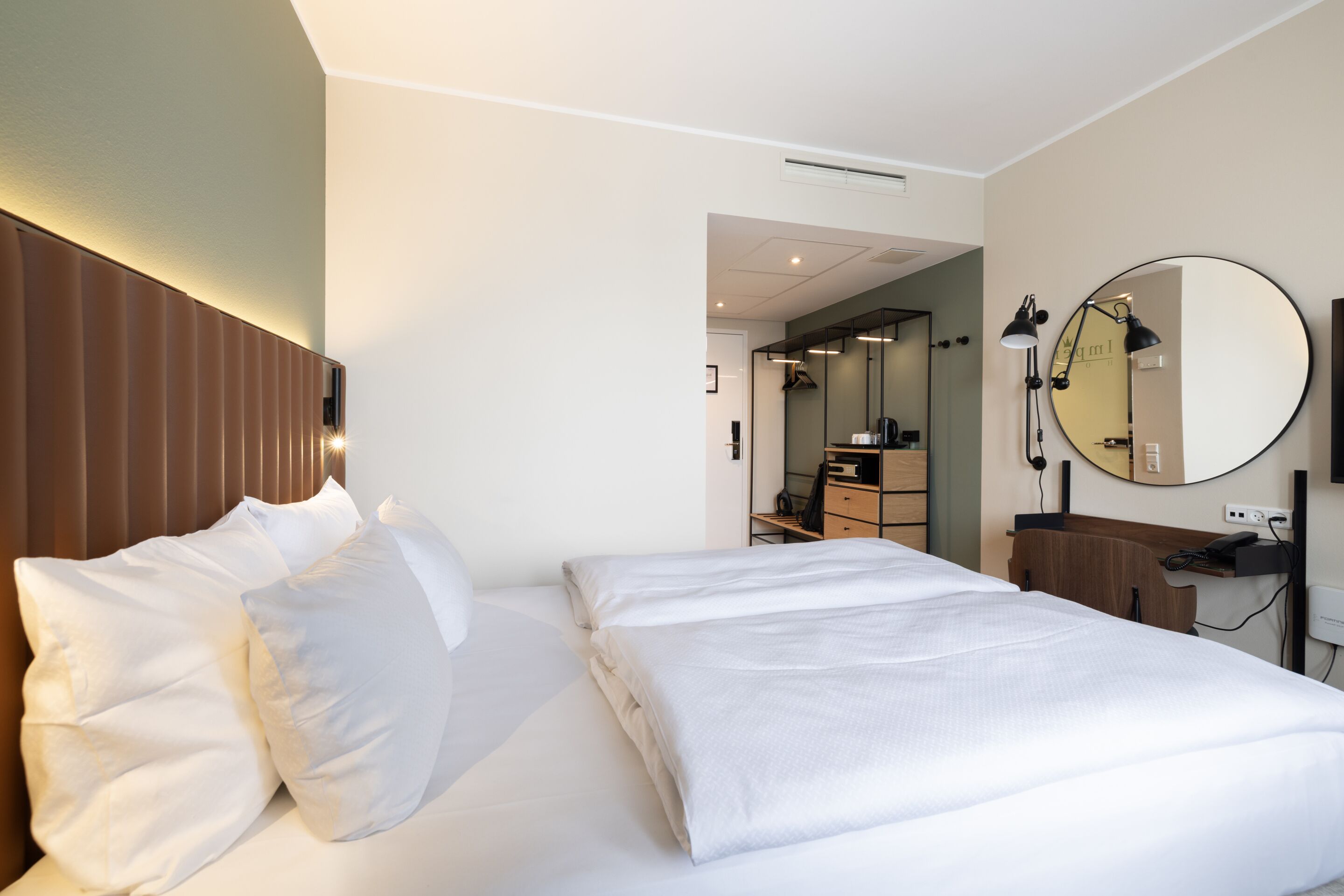 A hotel room with a bed, a bedside table, a mirror, and a wardrobe.