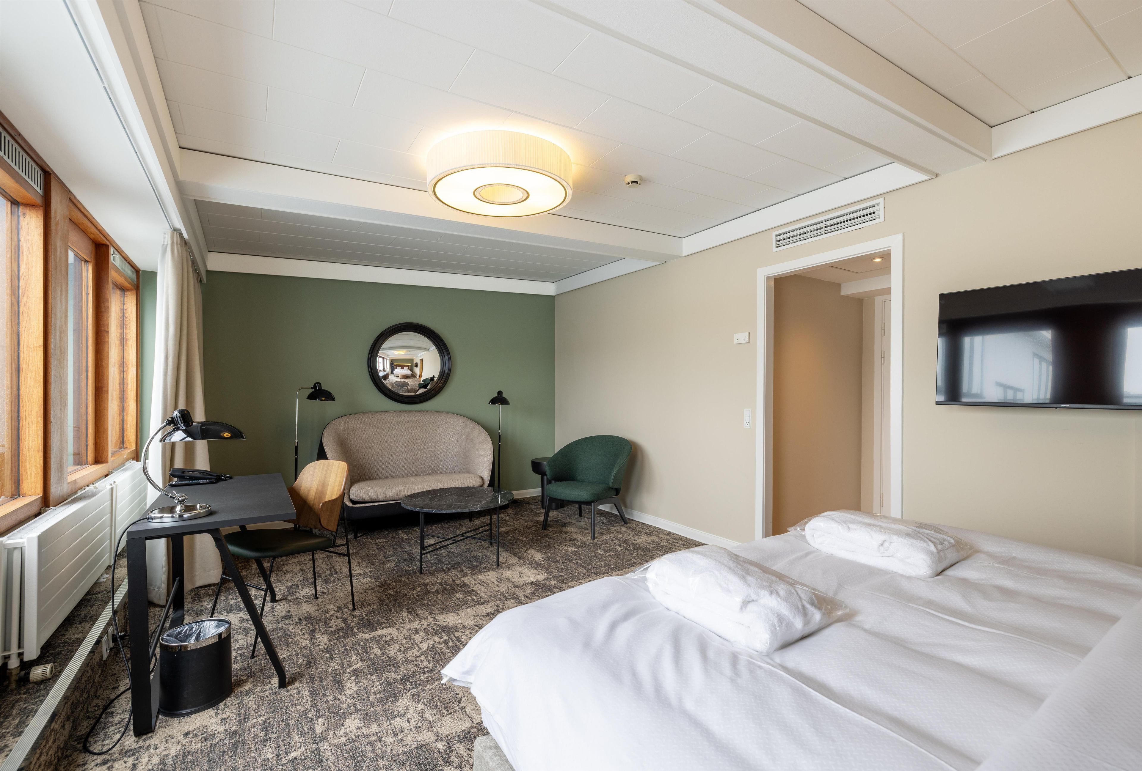 Habitación de hotel con cama, escritorio, dos sillas, espejo y televisor en la pared.