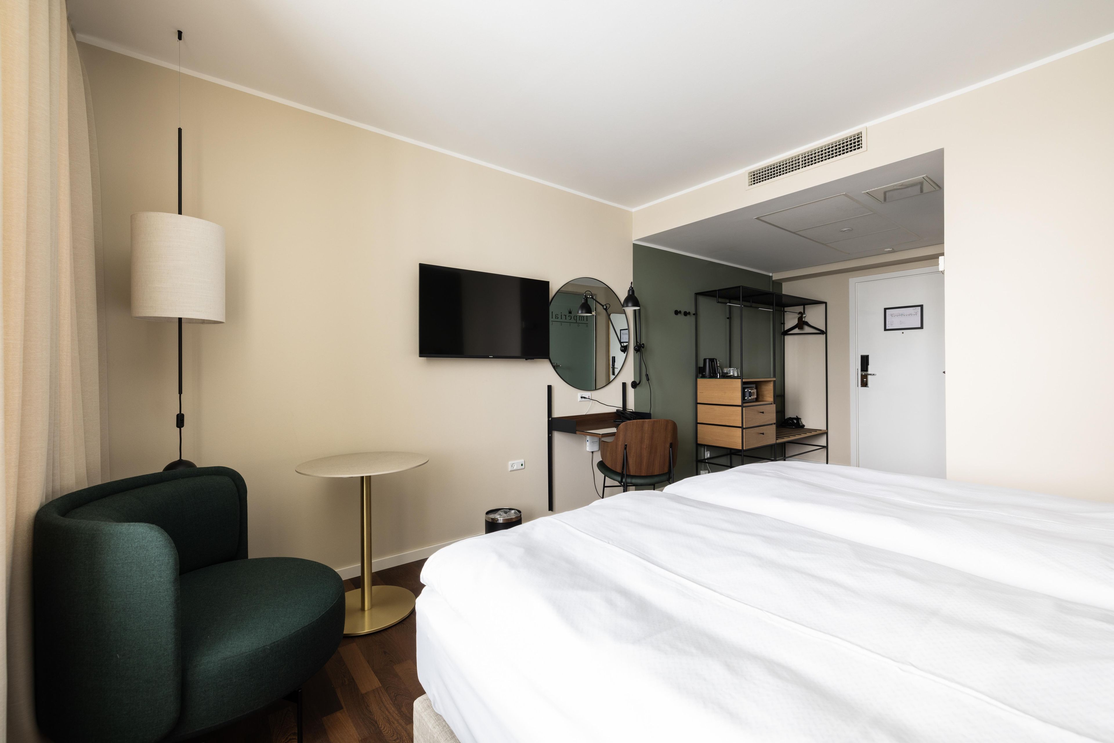 A hotel room with a bed, a desk, a chair, a TV, and a mirror.