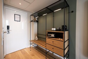 A hotel room with a wooden floor, a white door, a black metal shelf with a coffee maker, and a framed certificate on the wall. - Imperial Hotel (Copenhagen)