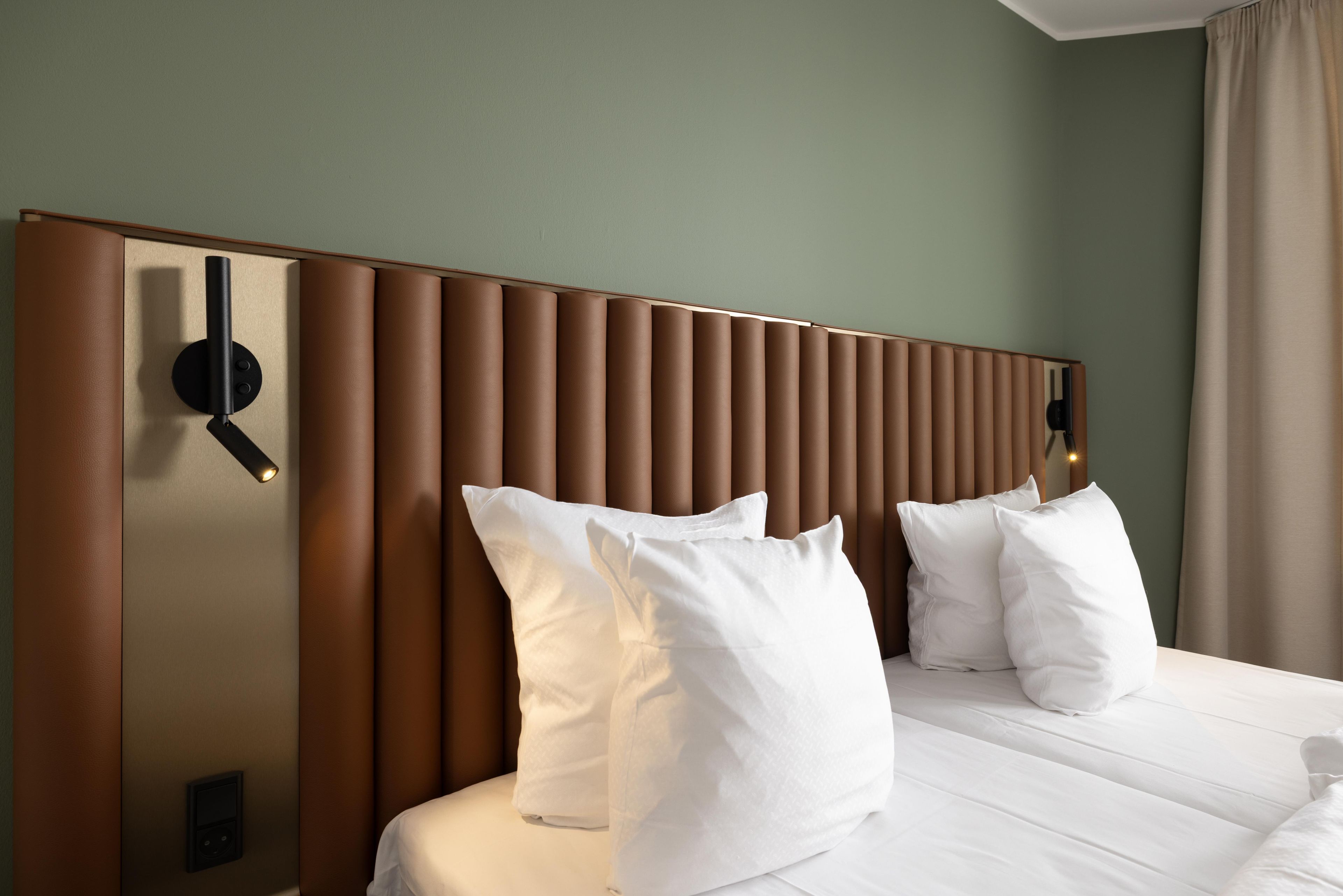 Una habitación de hotel con una cama grande, cabecera con listones verticales y una lámpara de pared.