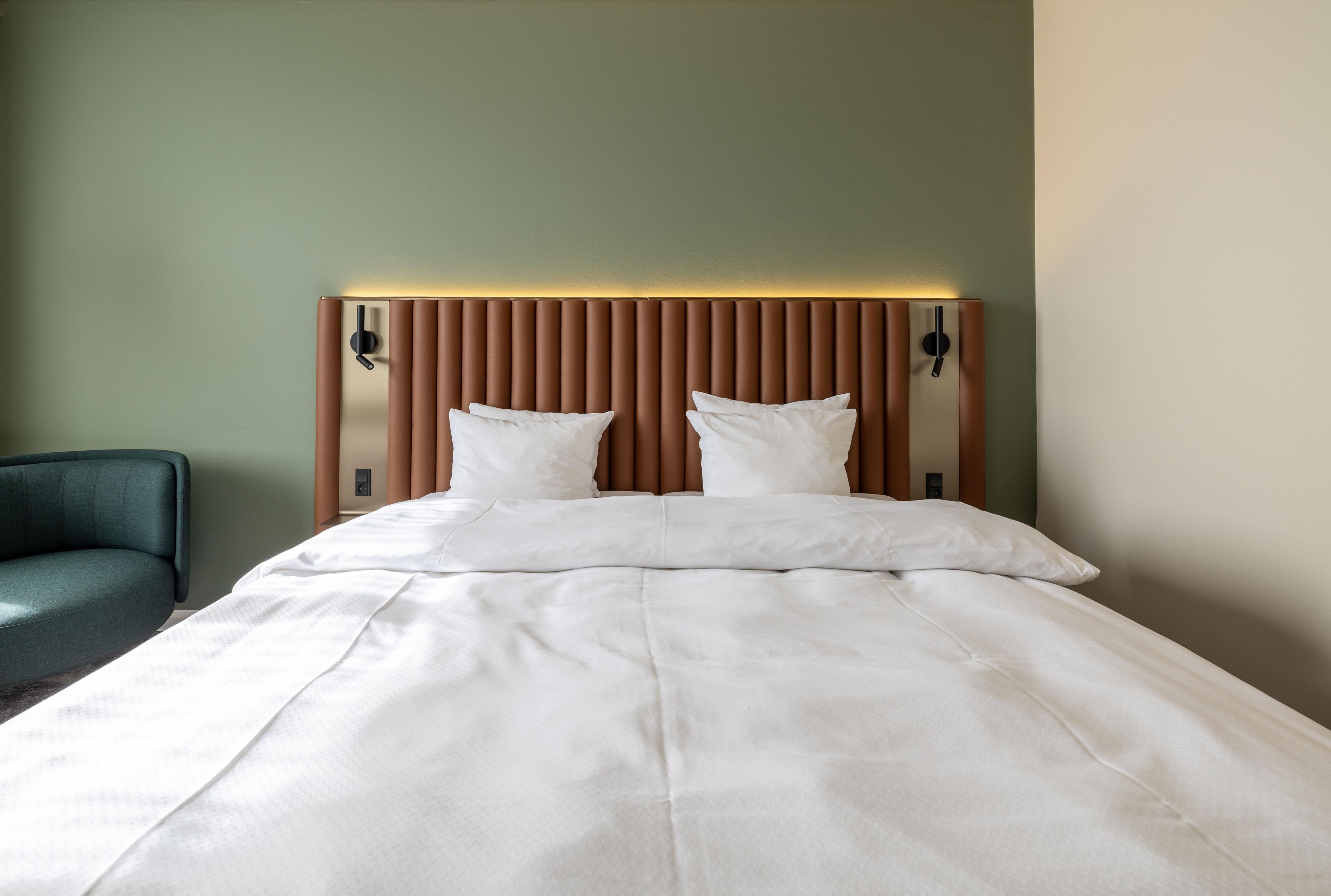 A hotel room with a bed, two bedside tables, and a green armchair.