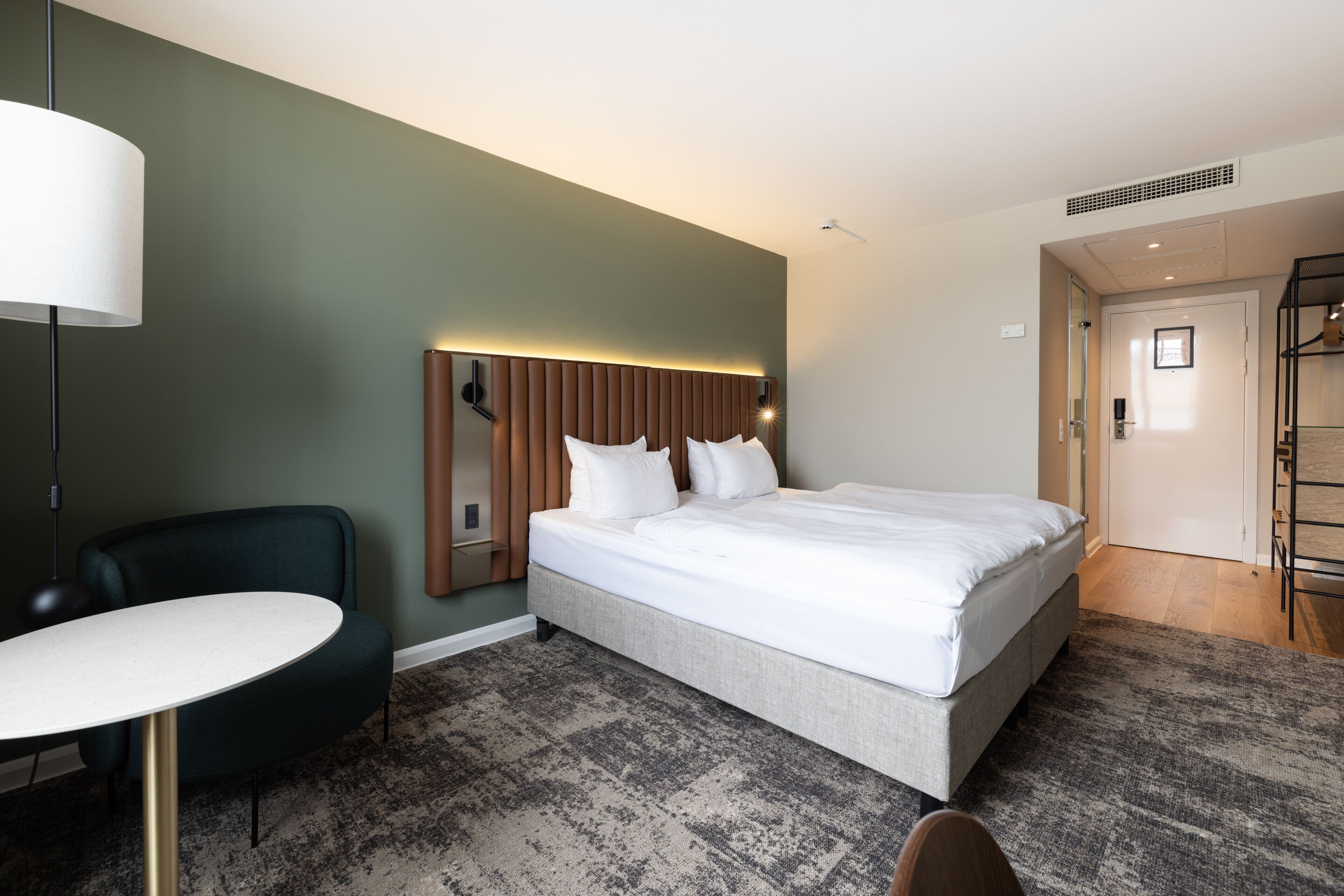 A hotel room with a bed, a desk, a chair, and a lamp.