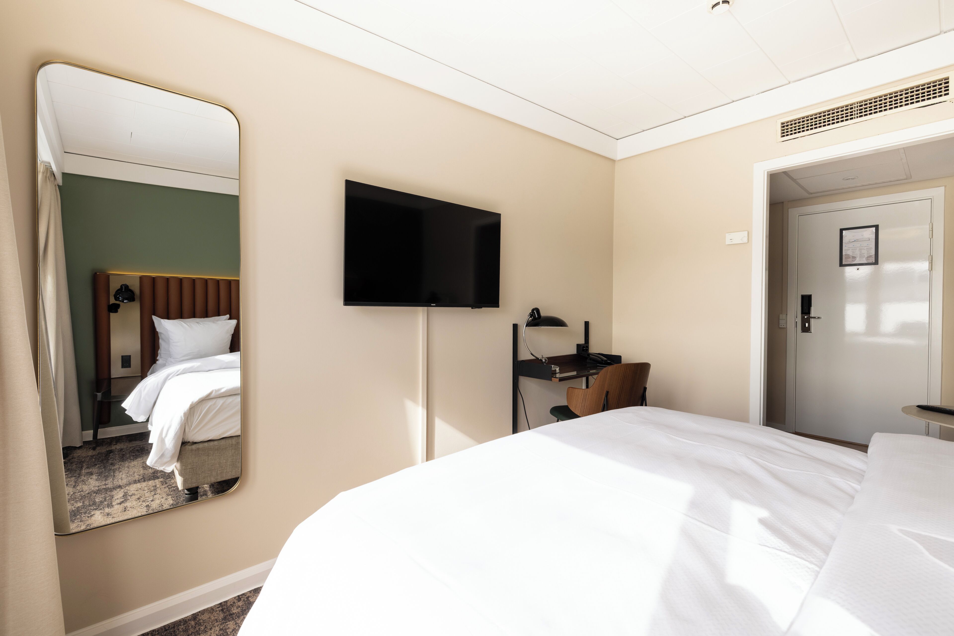Ett hotellrum med en stor säng, ett skrivbord med en stol, en platt-TV och en dörr.