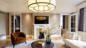 A living room with a fireplace, a sofa, a coffee table with books, and a large chandelier. - DoubleTree by Hilton Brussels City (Brussels)