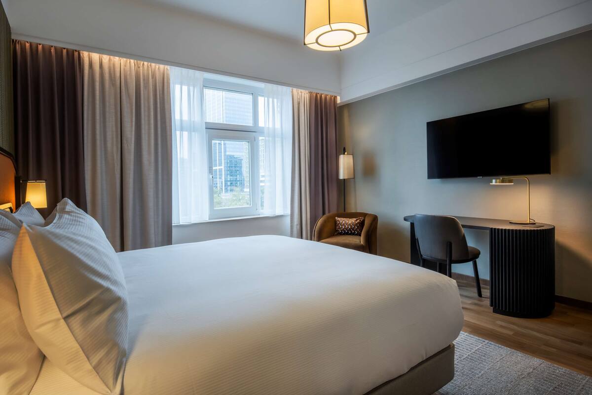 A hotel room with a large bed, a desk, a chair, a television, and a window with curtains.