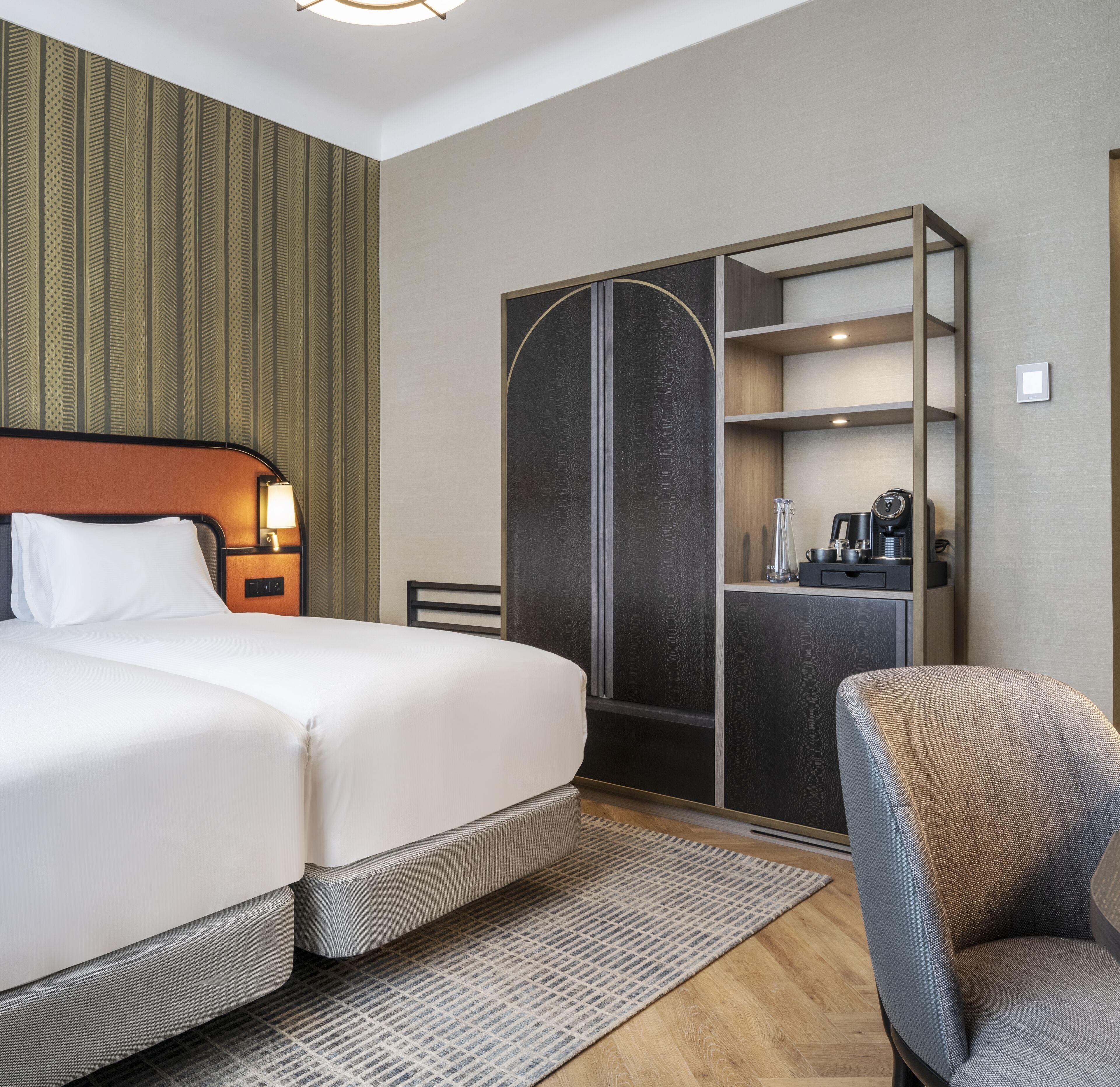 A hotel room with a bed, a wardrobe, a chair, and a coffee machine.