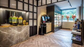 A modern hotel lobby with a marble reception desk, a self-service beverage station, a Wundermart store, and a refrigerated display.