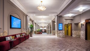 A hotel lobby with a red sofa, a large screen displaying information, and a hallway leading to elevators. - DoubleTree by Hilton Brussels City (Brussels)