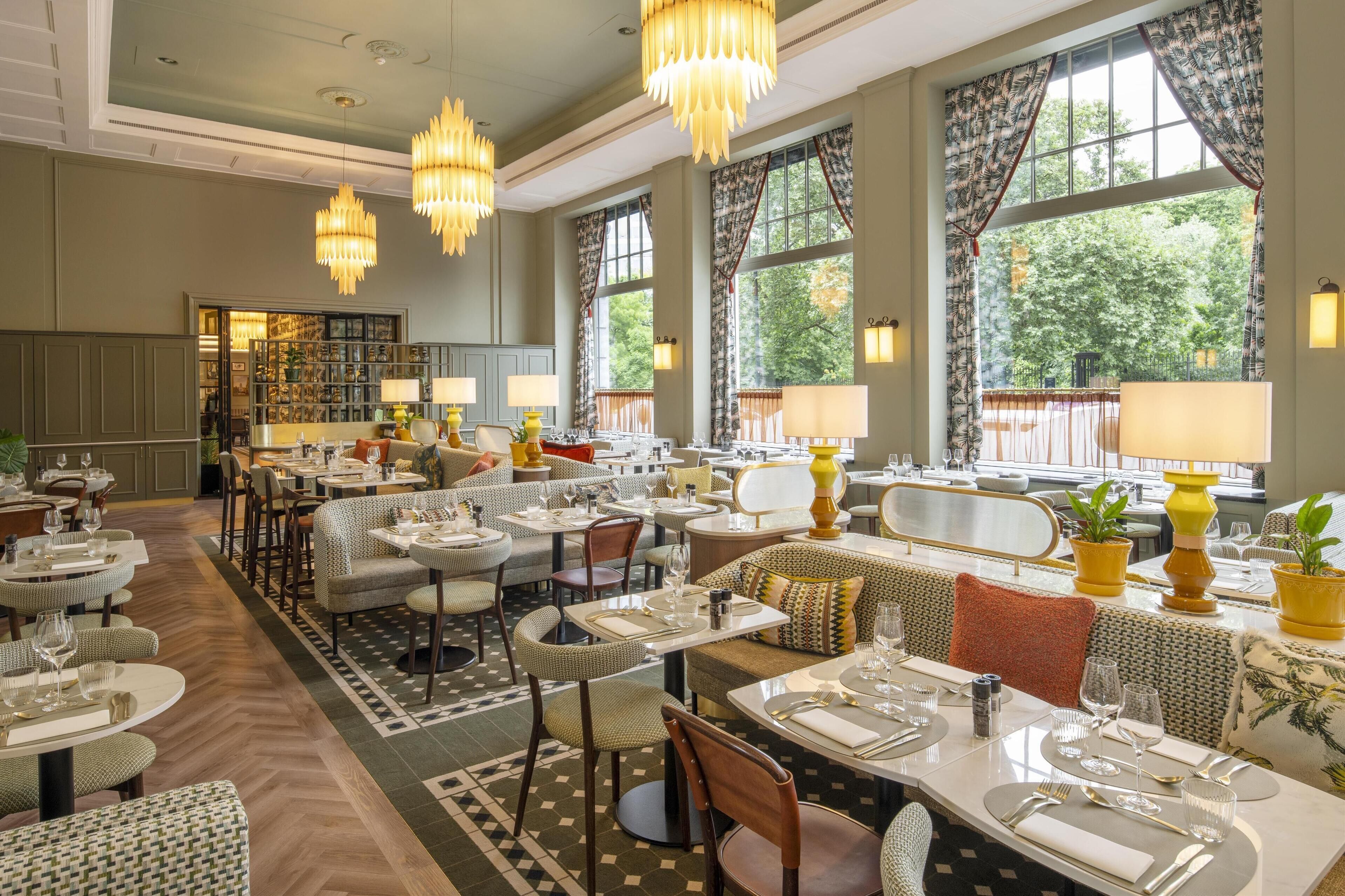 A spacious restaurant with multiple dining areas, chandeliers, and large windows offering views of the outdoors.