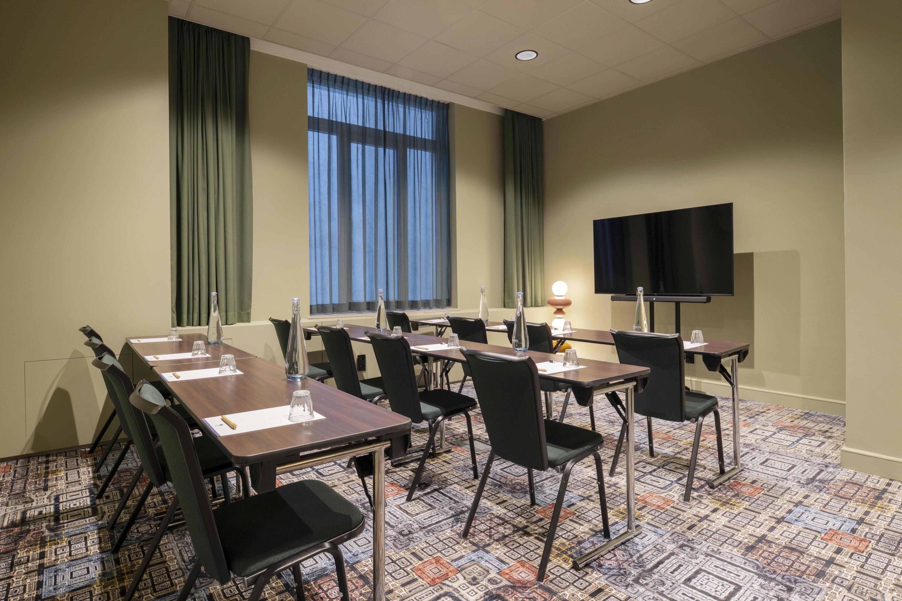 A conference room with tables, chairs, a TV, and a patterned carpet.