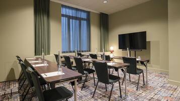 A conference room with tables, chairs, a TV, and a patterned carpet.