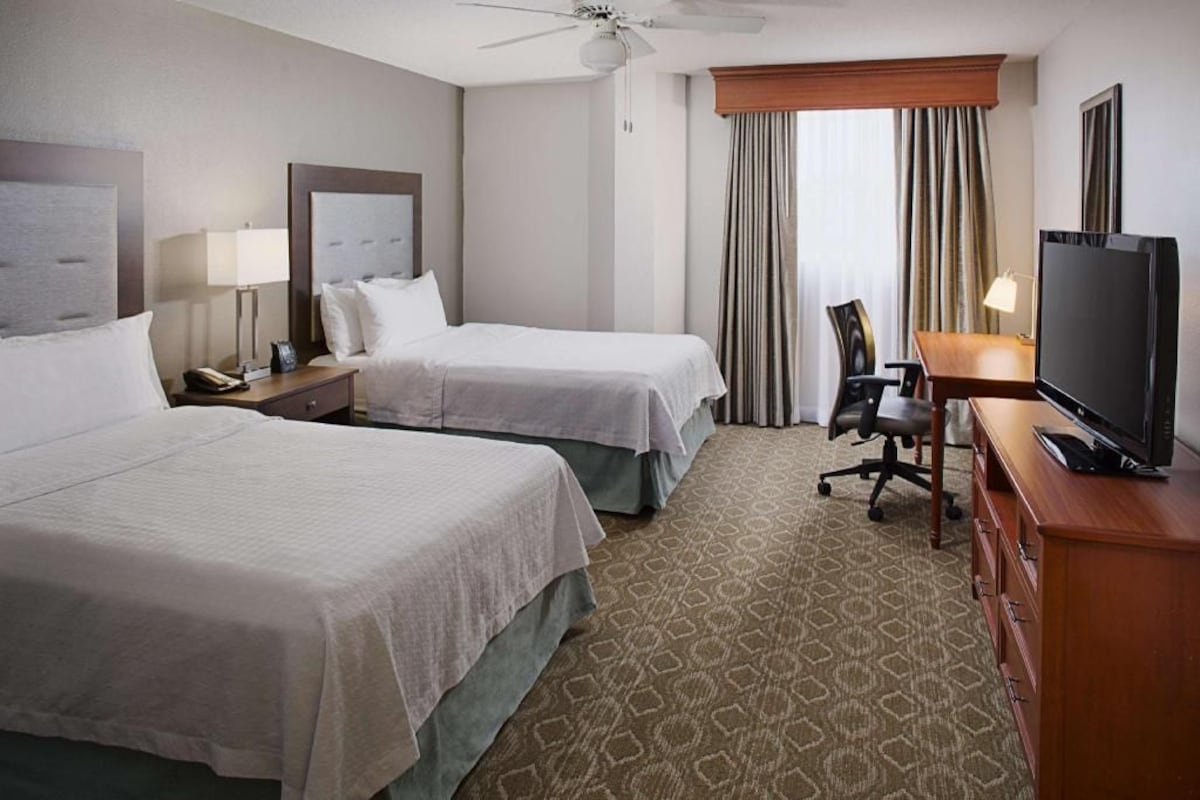A hotel room with two beds, a television, a desk, and a chair.