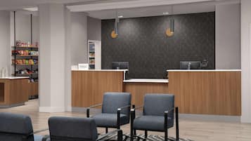 En moderne receptionsområde med en træreception, to grå stole, en lille reol med snacks og en mørk væg med et mønster.