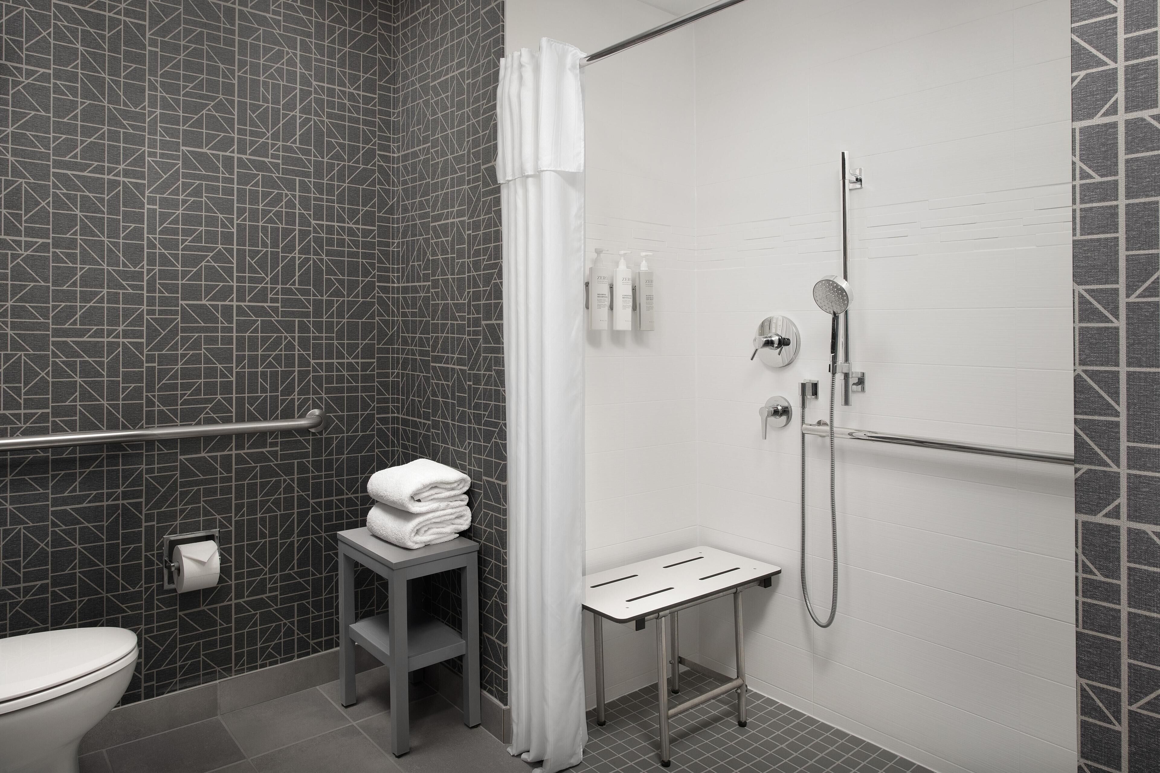 Un baño moderno con ducha, inodoro y una pequeña mesa con toallas.