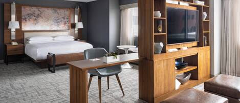 A modern hotel room with a large bed, a desk with a chair, a television, and a wooden entertainment unit.