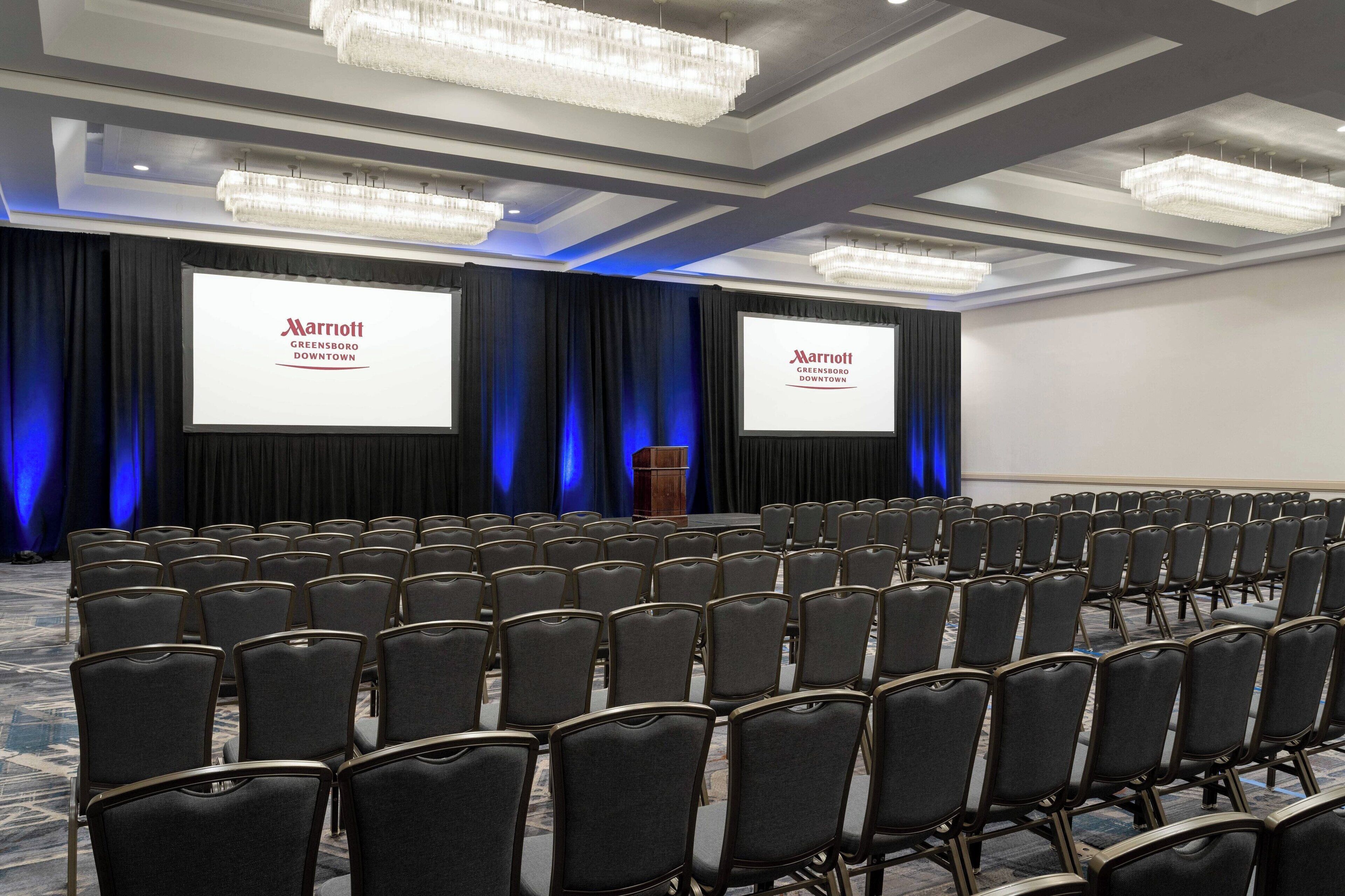 A conference room with rows of chairs, a stage with a podium, and two screens displaying the Marriott logo.