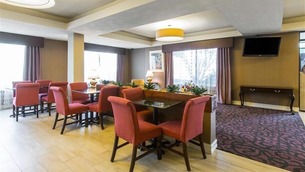 A hotel room with a dining area featuring a table and chairs, a flat-screen TV mounted on the wall, and a large window with curtains. - Royal Palms INN (Stockbridge)