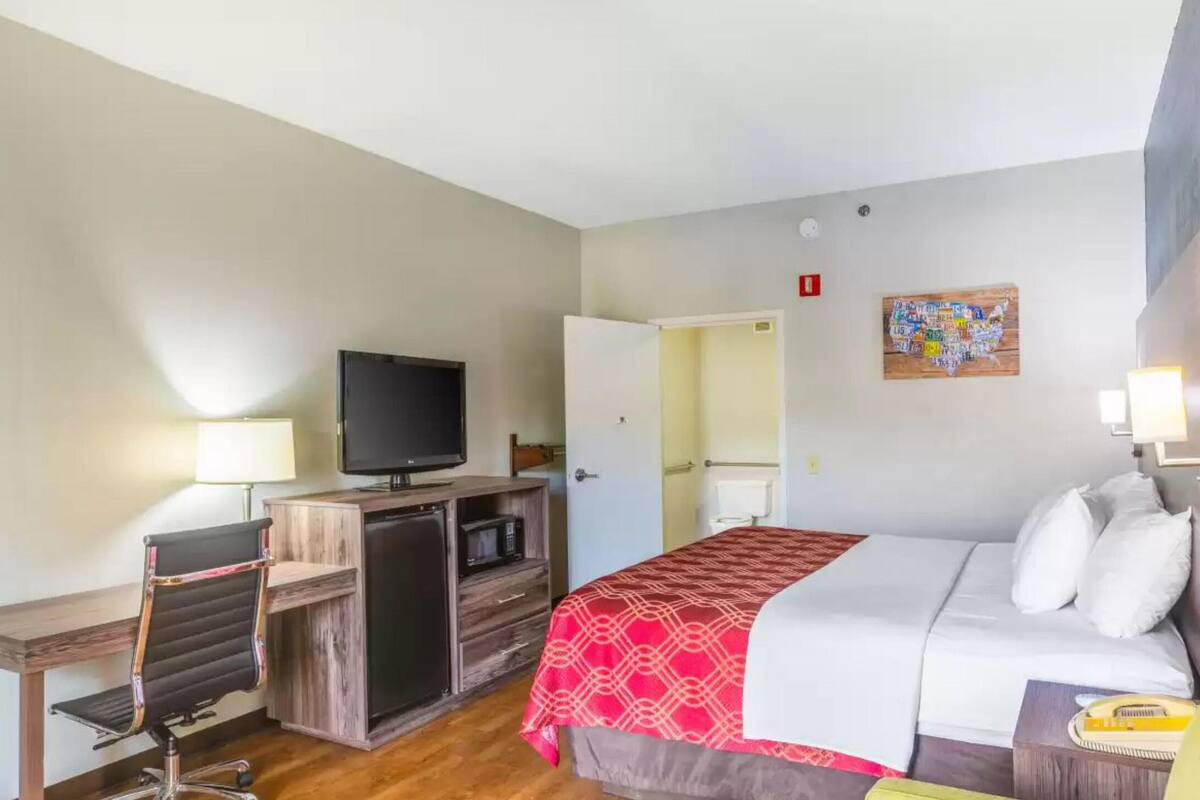 A hotel room with a bed, a desk with a computer, a television, and a door leading to a bathroom.