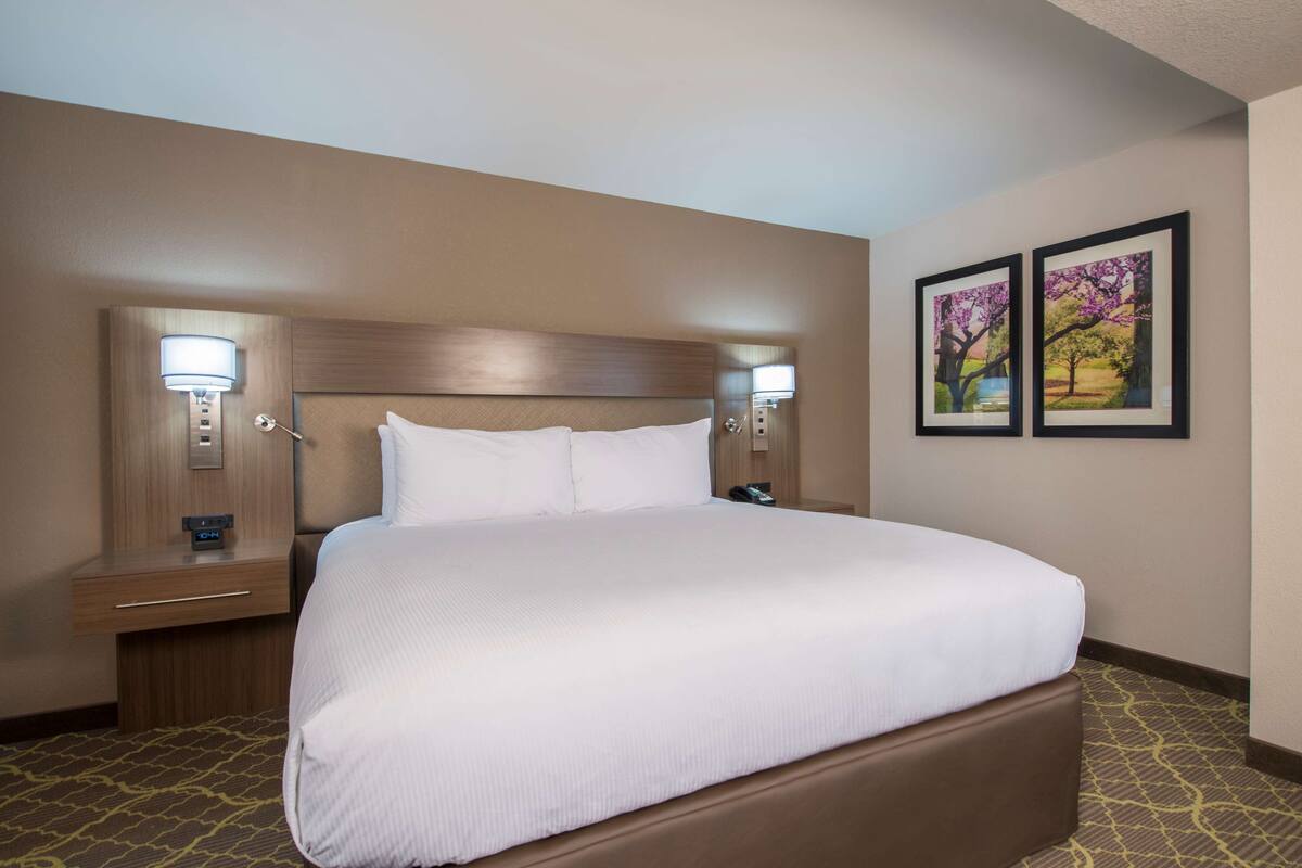 A hotel room with a large bed, two bedside tables with lamps, and two framed pictures on the wall.