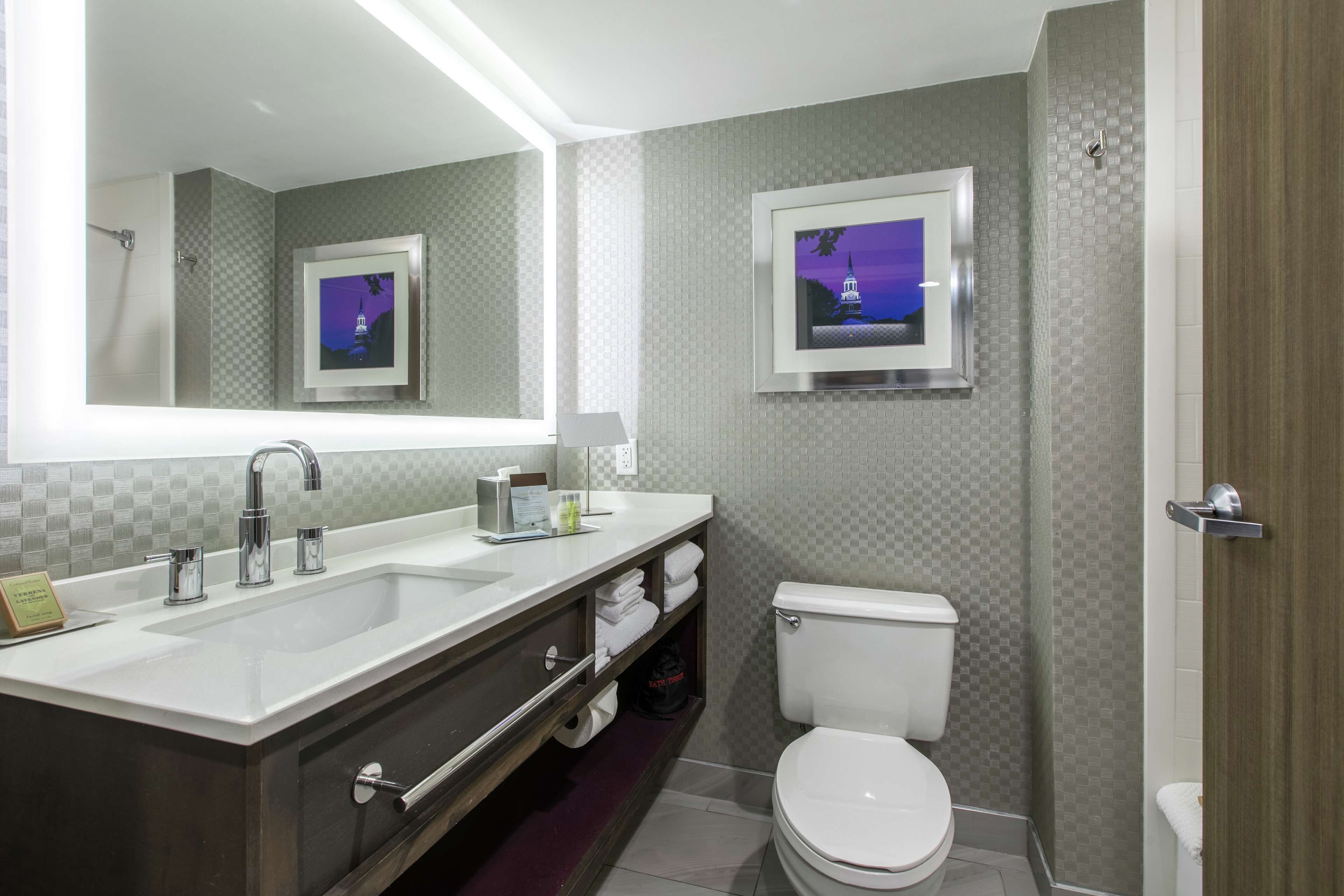 A modern bathroom with a large vanity, dual sinks, a toilet, and two framed pictures on the walls.