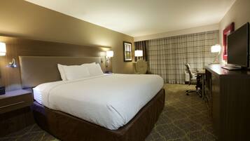 A hotel room with a large bed, a desk with a computer, a chair, and a TV.