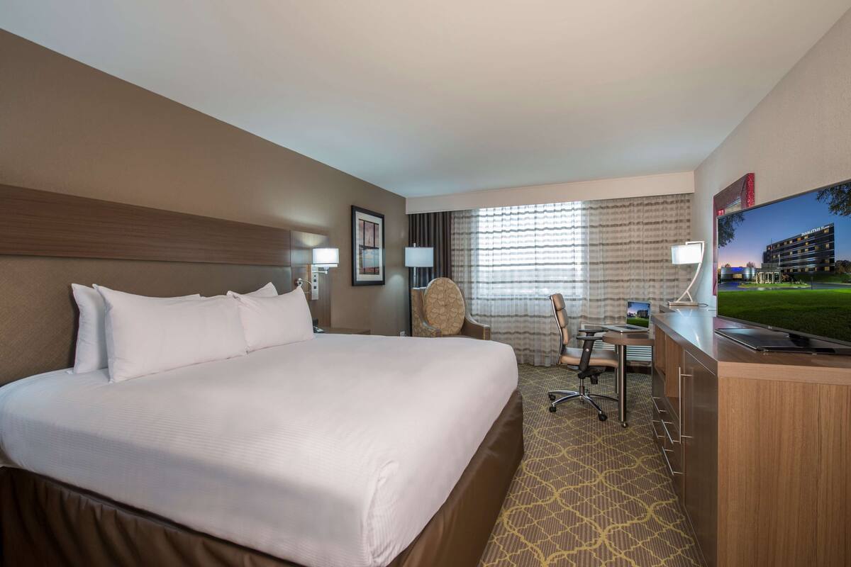 A hotel room with a large bed, a desk with a chair, a television, and a window with curtains.