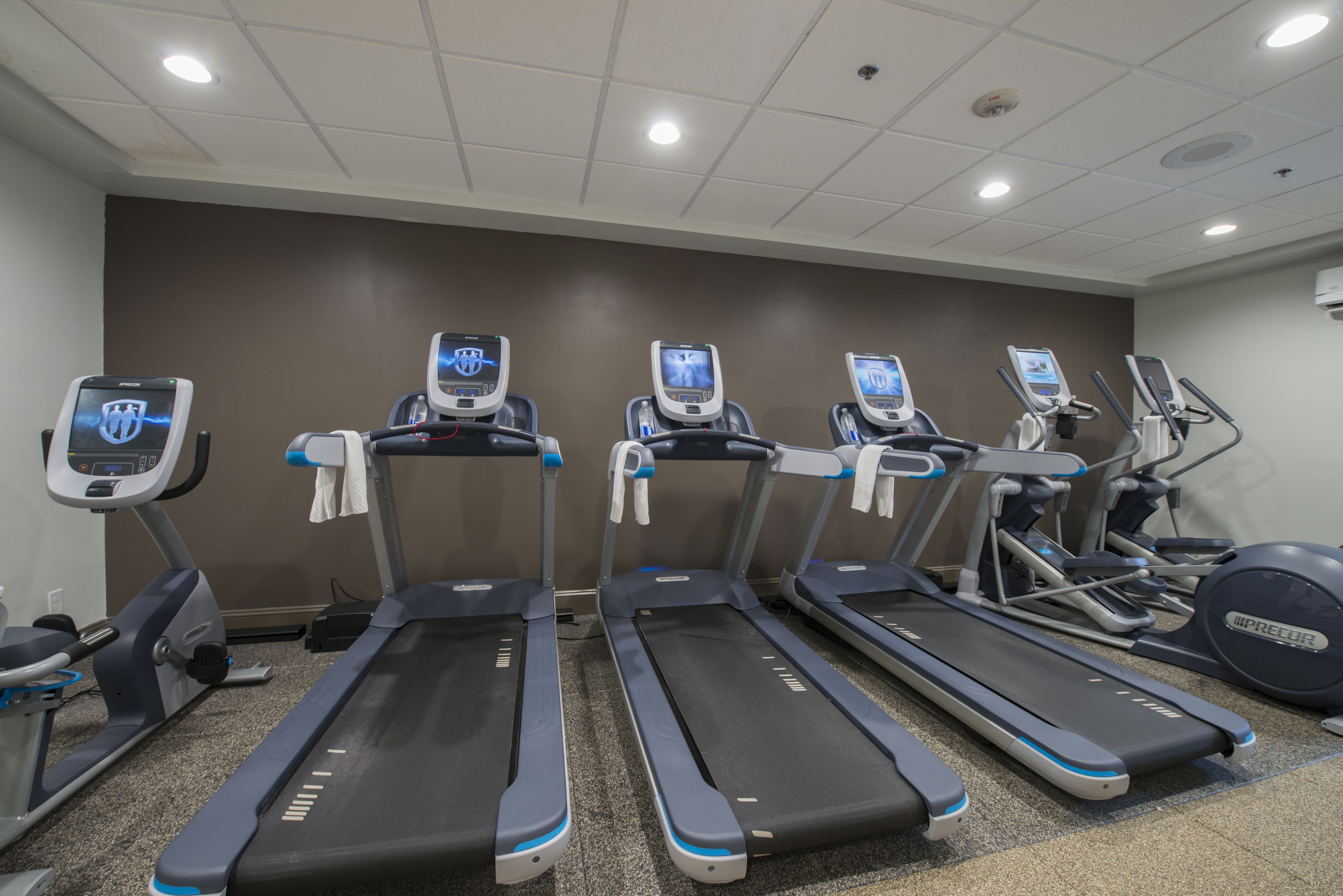 Un gimnasio con cintas de correr, elípticas y una bicicleta estática.