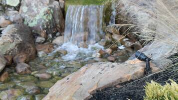 Ein kleiner Wasserfall in einem Garten mit Steinen und Pflanzen.