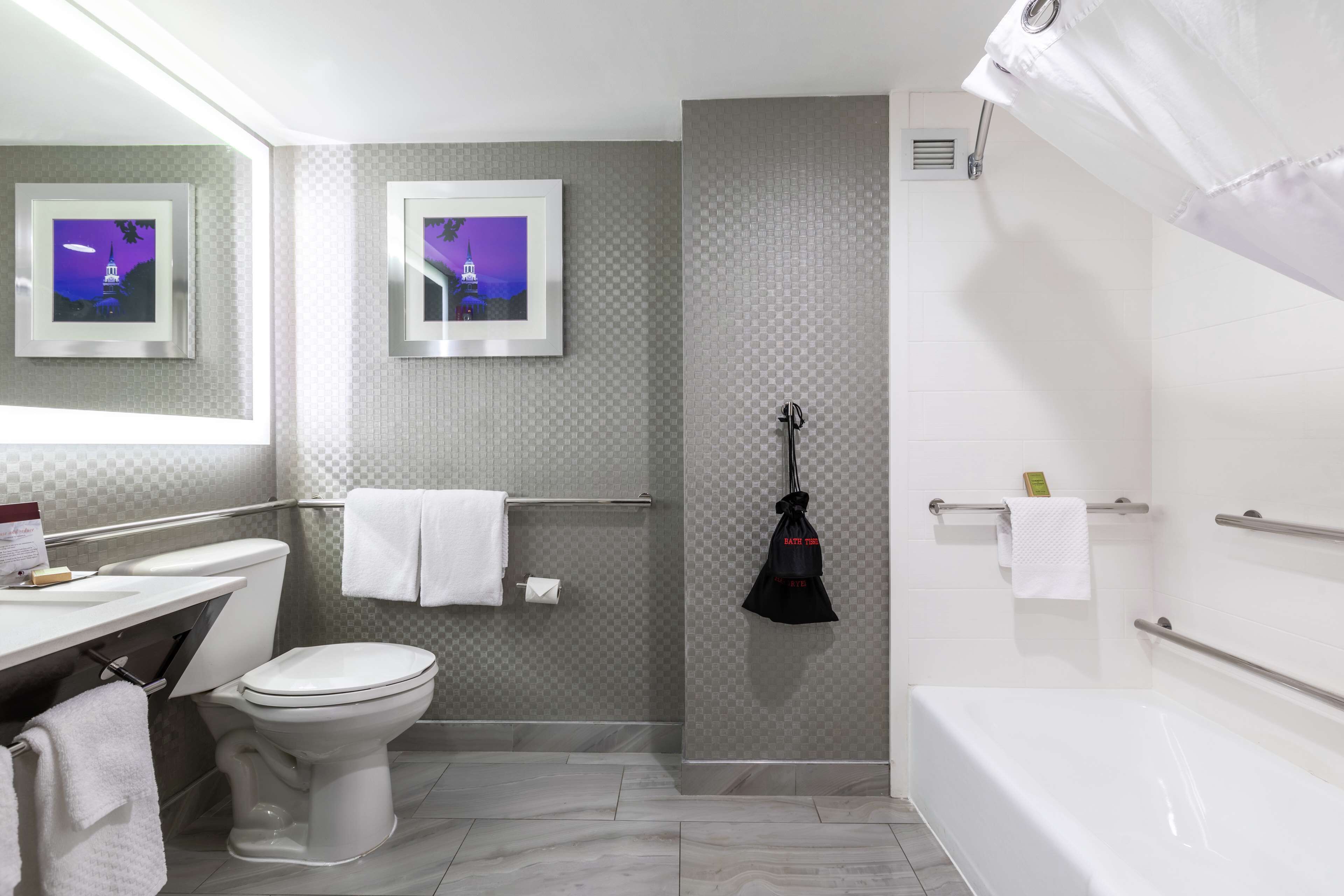 Un baño moderno con inodoro, lavamanos y bañera. Hay cuadros enmarcados en la pared y un perchero para toallas.