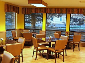 A restaurant with wooden tables and chairs, large windows with blinds, and a view of the street outside. - Horse Creek Inn (McCook)
