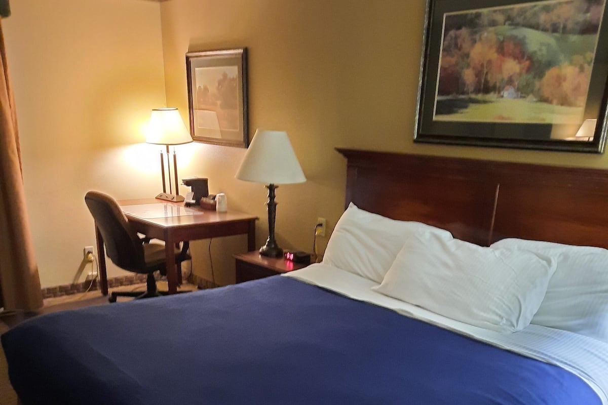 Ein Hotelzimmer mit einem großen Bett, einem Schreibtisch mit Lampe, einem Sessel und einem Bild an der Wand.