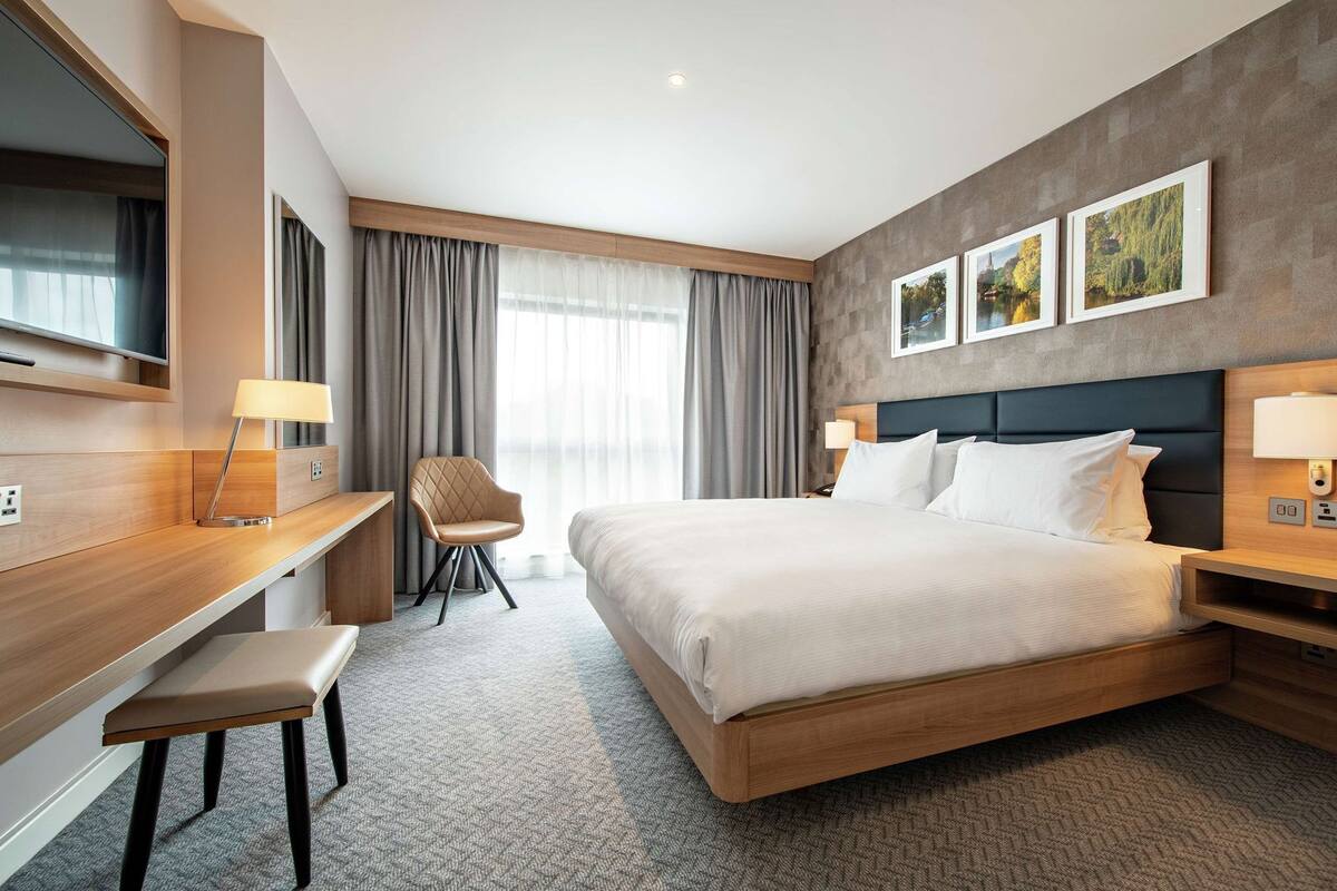 A modern hotel room with a large bed, a desk, a chair, and a TV.