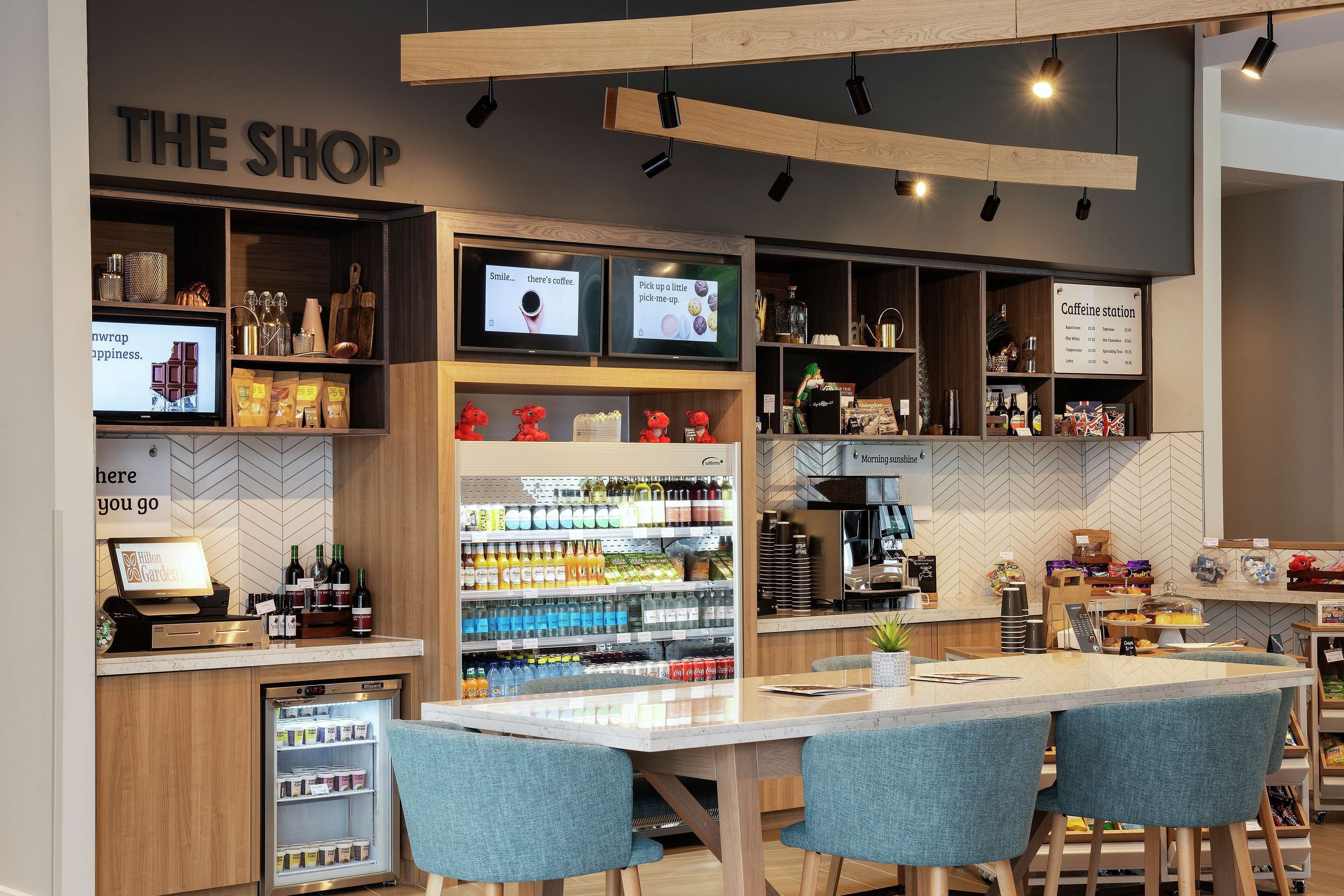 A modern coffee shop interior with a counter, seating area, and shelves stocked with coffee and snacks.