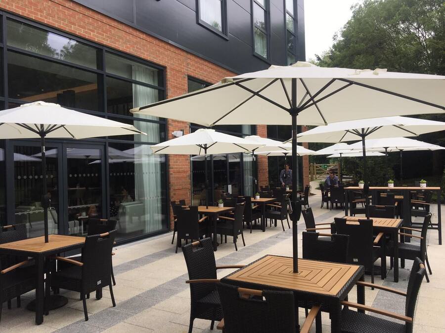 An outdoor patio area with multiple tables and chairs, large umbrellas, and a brick building in the background.